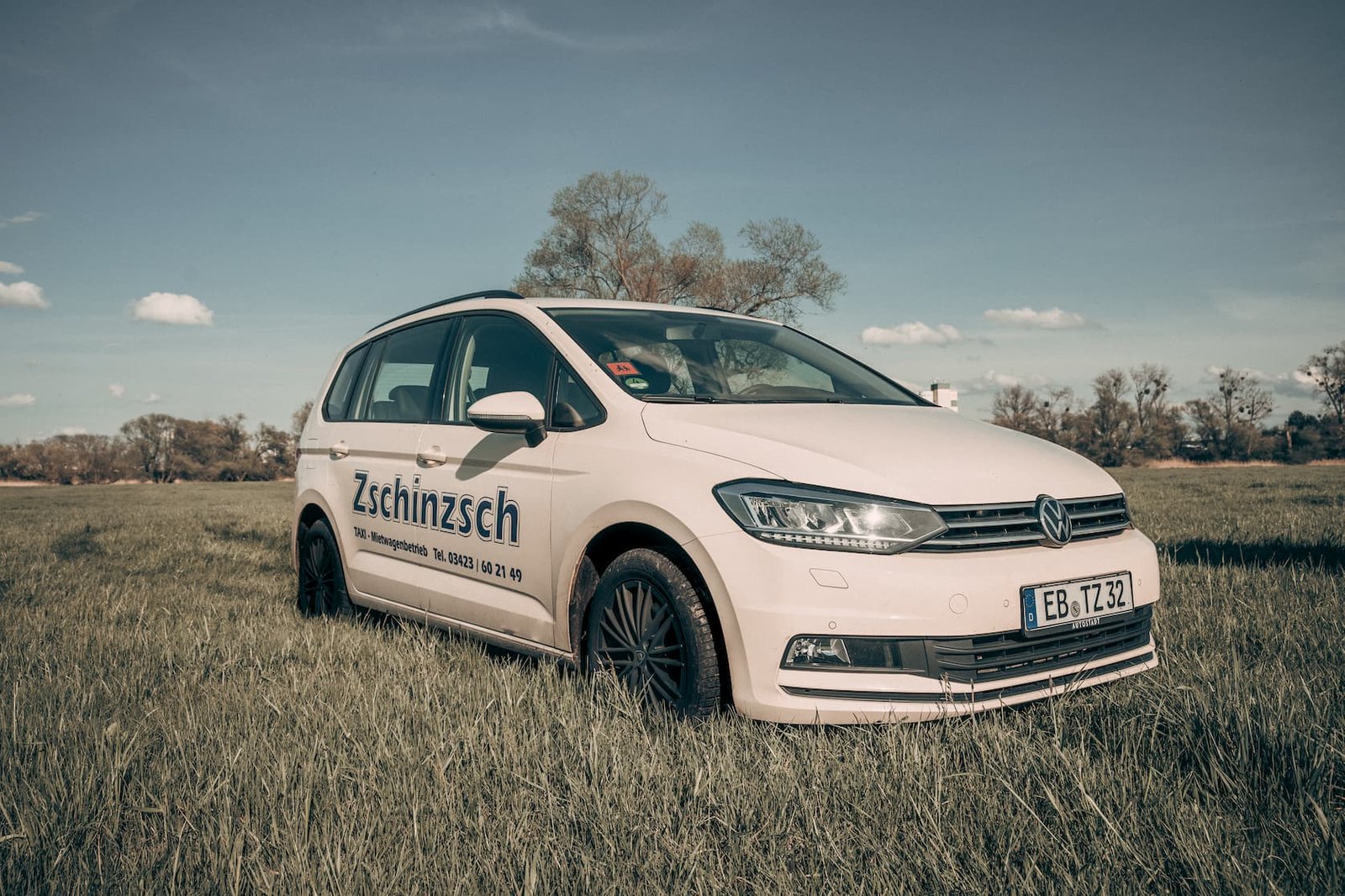 Weißer VW Touran von Taxi Zschinzsch mit Firmenbeschriftung auf einer Wiese